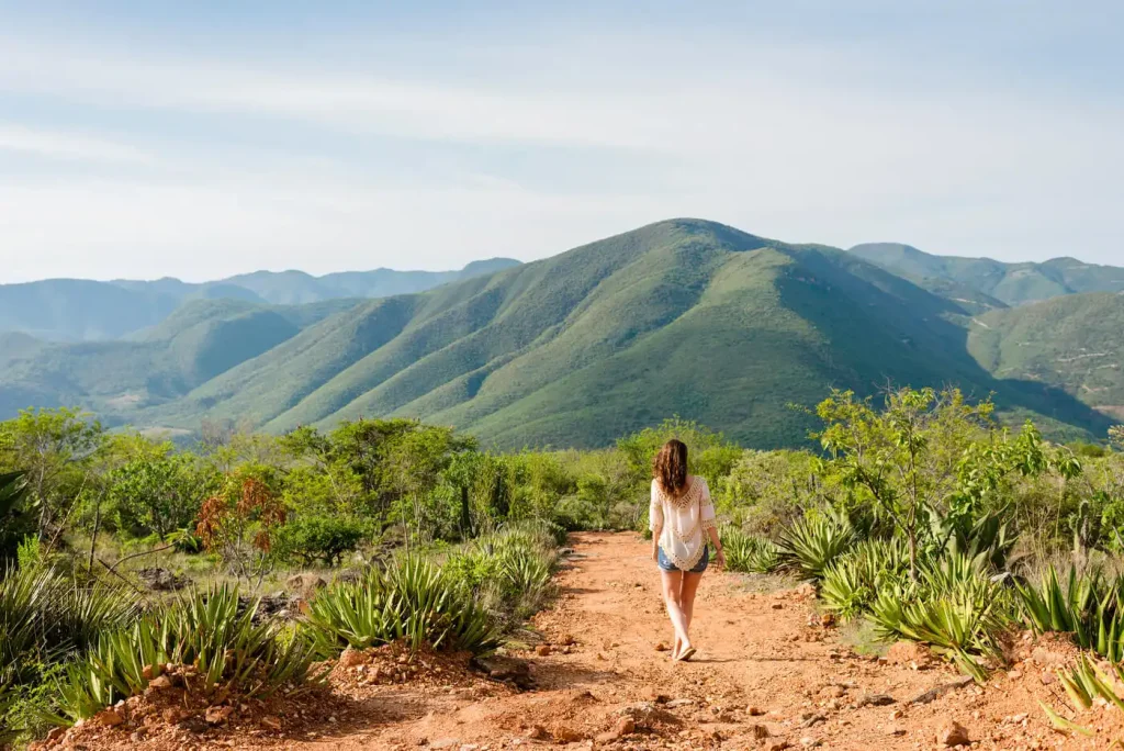 ¿Qué hora es en México, una chica viajera curiosa con un vestido blanco frente a una zona montañosa de un pueblo de México?